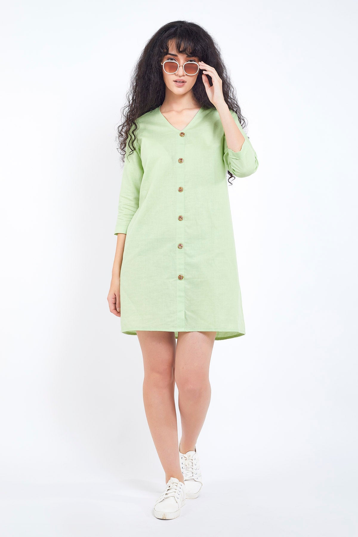A woman standing in a light green cotton linen mini dress with buttoned placket, three-quarter sleeves, and knee-length.