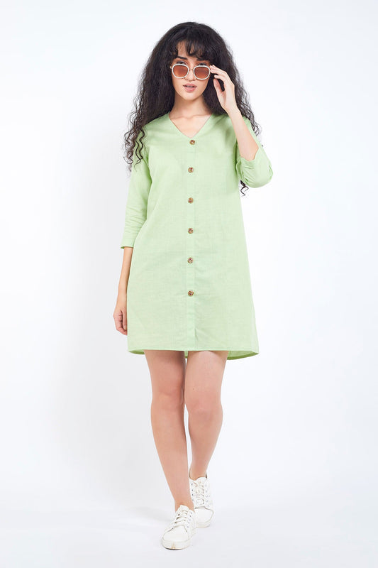 A woman standing in a light green cotton linen mini dress with buttoned placket, three-quarter sleeves, and knee-length.