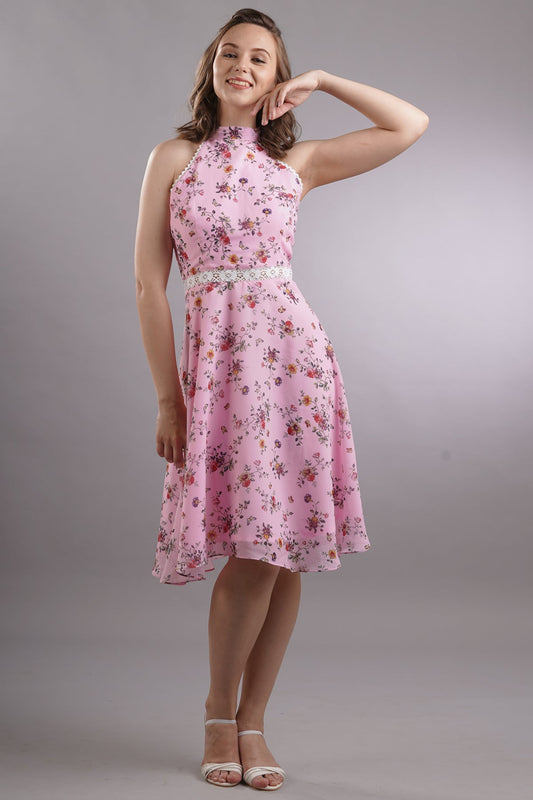 A woman wearing a pink floral printed halter neck knee-length dress with lace detailing and a back zip.